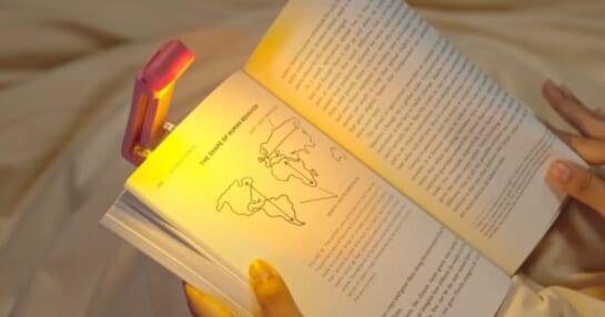 a book being held by a person with a pink clip on booklight lighting the text