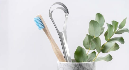 Tooth brush, tongue scraper and mint leaf right next to eachother