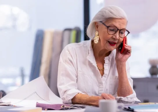 Older women talking on a cell phone at a desk with fabric swatches